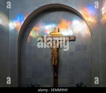 Kruzifix-Statue in der Nische der Kirche mit farbigem Licht aus Buntglas Stockfoto