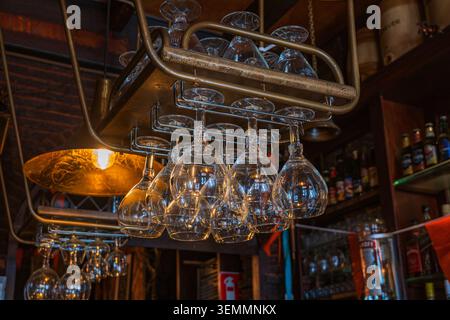 Amsterdam, Niederlande, 22.04.2026 - Weingläser hängen auf einem Regal über einem Bartheken in einem traditionellen niederländischen Pub in zaandam, gemütliches warmes Licht i Stockfoto