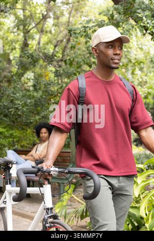 Afroamerikanisches Paar, das auf einer Bank im grünen Park sitzt, Mann mit weißem Straßenfahrrad Stockfoto