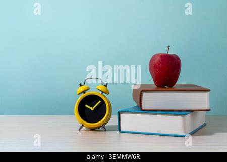 Ein roter Apfel auf einem Stapel von zwei Büchern neben einem gelben Wecker auf einem Holztisch. Bildung, Back-to-School-Themen, Zeitmanagement, Lernen Stockfoto