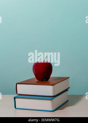 Eine vertikale Komposition mit einem roten Apfel auf einem Stapel von zwei Büchern. Kopierbereich für Text. Bildung, Schulanfang, Lernkonzept. Stockfoto