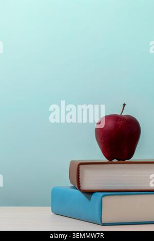 Eine vertikale Komposition mit einem roten Apfel auf einem Stapel von zwei Büchern. Kopierbereich für Text. Bildung, Schulanfang, Lernkonzept. Stockfoto