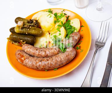 Gebratene Würstchen mit hausgemachten gekochten Kartoffeln und Gurken Stockfoto