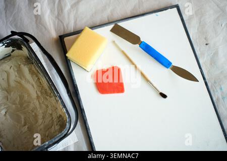 Kunstwerkzeuge, Schwamm und Gipspaste liegen auf Leinwand am Tisch, Draufsicht. Konzept mit strukturierter Wandkunst, handgefertigter Einrichtung und kreativem Hobby. Stockfoto