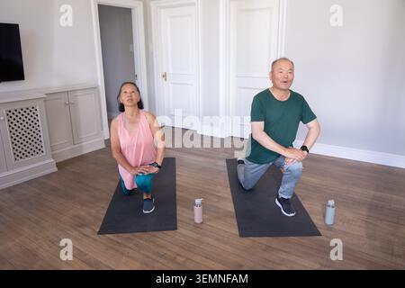 Asiatisches Paar kniet und dehnt sich auf schwarzen Matten auf Hartholzboden mit Wasserflaschen, Uhren Stockfoto