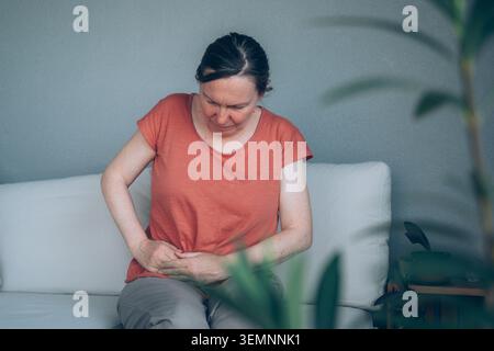 Reife Frau, die auf einem Balkonsofa sitzt und den rechten Unterbauch mit Schmerzen hält. Das Konzept von Appendizitis-Symptomen, Bauchbeschwerden und Gesundheitsproblemen. Stockfoto