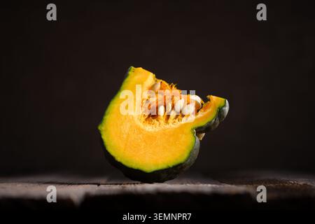 Einzelne Kürbisscheibe auf rustikalem Holztisch mit dunklem Negativraum. Minimales Herbststillleben mit Kürbis und stimmungsvollem Erntestil Stockfoto