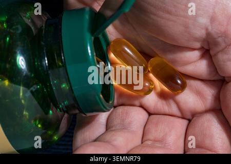 Fischöl Omega 3 Kapseln aus der Flasche in die Hand gießen. Nahaufnahme einer Person, die bernsteinfarbene Omega-3- oder Vitamin-e-Kapseln aus einem grünen Kunststoff gießt Stockfoto