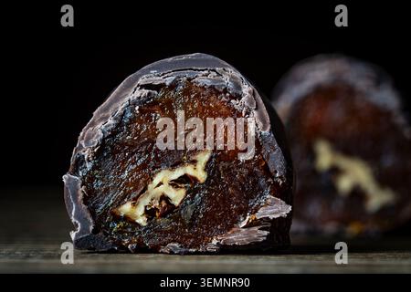 Schokoladenüberzogene getrocknete Aprikosen mit Walnusskreuz Nahaufnahme. Makro aus zwei Schokoladenbonbons, gefüllt mit getrockneten Aprikosen und Walnuss Stockfoto