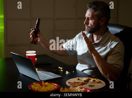 Mann, der spät im Büro arbeitet. Geschäftsmann, der spät arbeitet und Online-Inhalte ansieht. Freiberuflicher Mitarbeiter, der bis spät in entspannter Stimmung arbeitet. Mann, der spät arbeitet und genießt Stockfoto