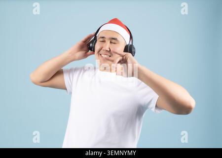 Fröhlicher junger Mann mit weihnachtsmann, der Musik in Kopfhörern hört Stockfoto