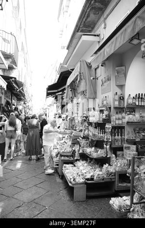 Schwarzweiß-Foto von Touristen, die in einer engen Straße im historischen Zentrum von Sorrent, Kampanien, Italien, in einem Limoncello- und Souvenirladen stöbern. Stockfoto