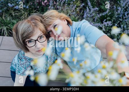Seniorenmutter und erwachsene Tochter nehmen Selfie unter Daisy Flowers Stockfoto