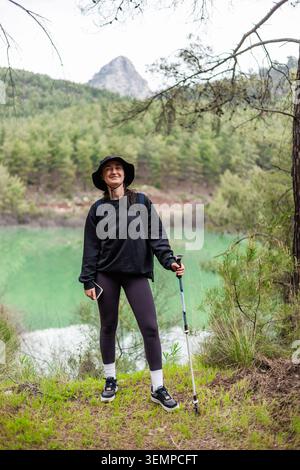 Glückliche junge Frau, die in der Nähe eines Bergsees wandert Stockfoto