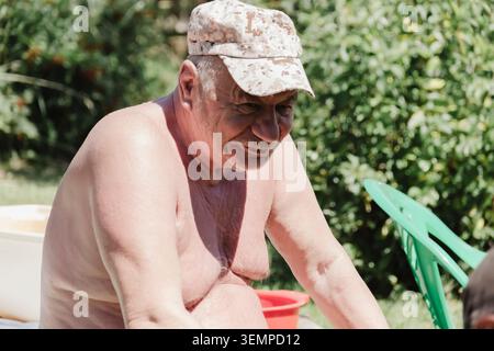 Ein älterer Mann sitzt im Hinterhof seines Hauses und sonnt sich, er hat Kopfschmerzen. Der ältere Mann ist depressiv, verärgert und denkt an die Jahre Stockfoto