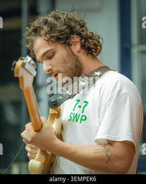 Ein junger Mann mit lockigen Haaren konzentriert sich auf das Gitarrenspielen Stockfoto