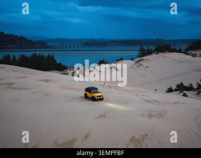 Der hellgelbe SUV erkundet die Sanddünen in der Dämmerung Stockfoto