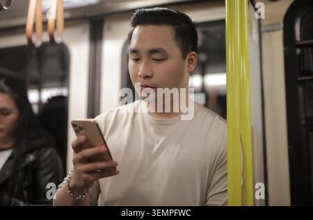Ein junger asiatischer Mann, der sein Handy in der U-Bahn überprüft Stockfoto
