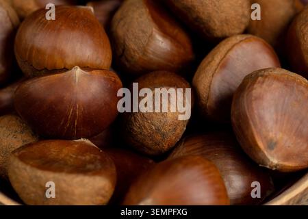 Hellbraune Kastanien in Geschirr, eine volle Schüssel mit Kastanienfrüchten steht auf strukturiertem Holz in der rustikalen Küche. Stockfoto