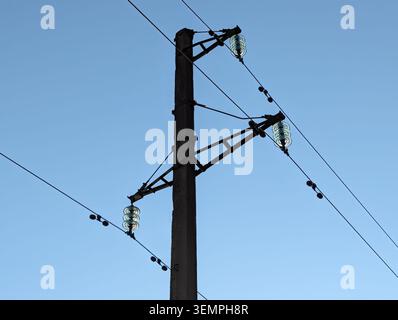 Silhouette der Hochspannungsleitung. Niedriger Winkel von Isolierelementen aus Glas und elektrischen Kabeln auf einem hohen Betonmast vor blauem Himmel Stockfoto