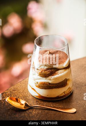Ein mehrschichtiges italienisches Tiramisu-Dessert in einer klaren Glasschale, das Schichten Mascarponcreme und kaffeespezialgetränkte Marienfinger zeigt, die mit Kakaopulver bestäubt sind. Stockfoto