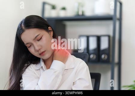 Asiatische Frau, die an Nackenschmerzen am Schreibtisch im Büro leidet Stockfoto