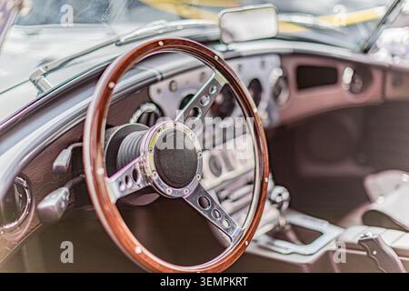 Oldtimer-Innenraum mit Holzlenkrad mit Mittelnabe in Metallic und elegantem, modernem Armaturenbrett mit kreisförmigen Zifferblättern und Messinstrumenten sowie Leder Stockfoto
