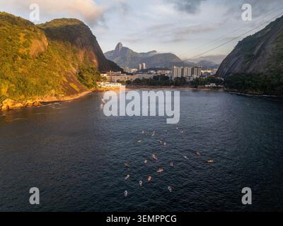 Blick aus der Vogelperspektive auf den Roten Strand mit Personen auf Paddleboards im Wasser, umgeben von steilen Hügeln und Bergen in Rio de Janeiro, Bundesstaat Rio de Janeiro, Stockfoto