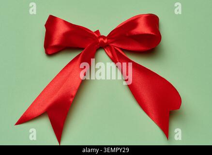 Eine üppig rote Satinschleife aus einem breiten Band in der Mitte des Rahmens auf olivgrünem Hintergrund, ein festliches minimalistisches Dekorationselement in Nahaufnahme Stockfoto