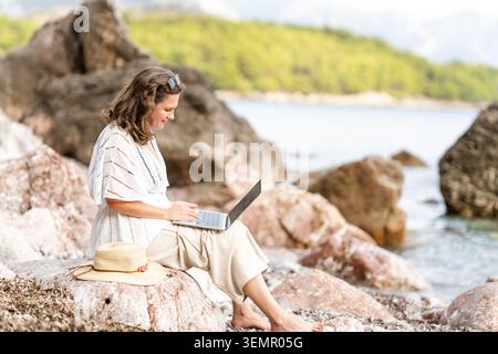Weibliche Freiberuflerin mit Laptop an der Küste Stockfoto