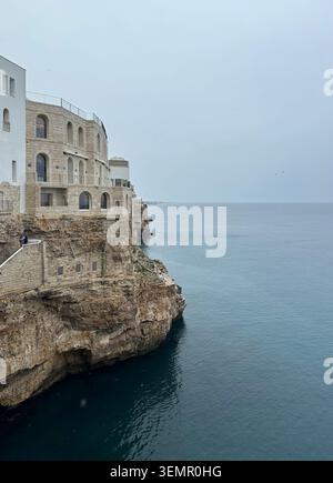 Gebäude aus hellem Stein stehen auf zerklüfteten Klippen in Polignano a Mare, Apulien, Italien. Die Architektur verfügt über bogenförmige Fenster A Stockfoto