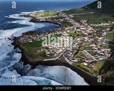 Blick aus der Vogelperspektive auf das Küstendorf Mosteiros mit weißen Häusern, grünen Feldern und einem schwarzen Sandstrand entlang der zerklüfteten Atlantikküste in Mosteir Stockfoto