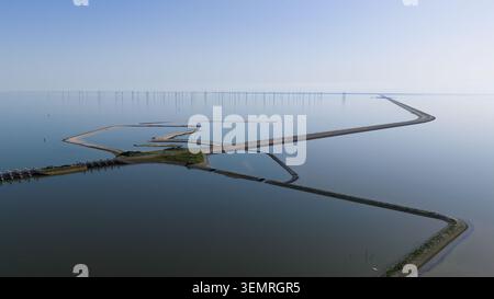 Luftaufnahme des Fischwanderungsprojekts Vismigratierivier und des Afsluitdijk-Deiches mit Windturbinen am Horizont unter klarem Himmel in Kornwerder Stockfoto