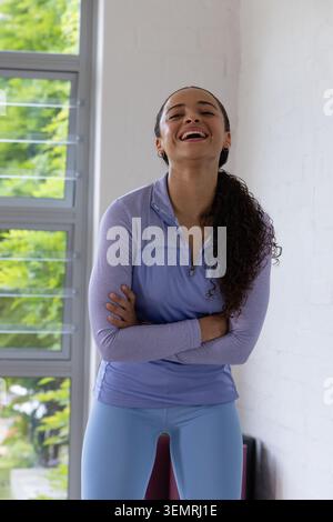 Erwachsene afroamerikanische Frau lacht im Studio am Fenster mit hellviolettem Sporttop Stockfoto