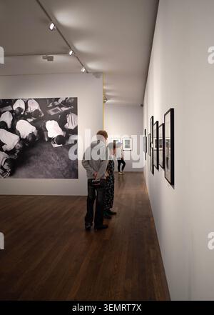 In der Fotografen Gallery, Ramillies Street, Central London. Ausstellungsbesucher studieren eine Reihe von gerahmten Fotografien im weißen Galerieraum. Stockfoto