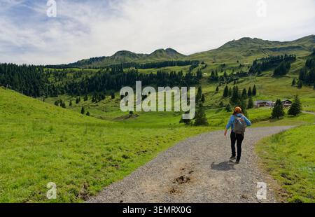 Wanderer folgt einem gewundenen Pfad durch die sanften Almwiesen von Stoos unter den Gipfeln der Zentralschweiz Stockfoto