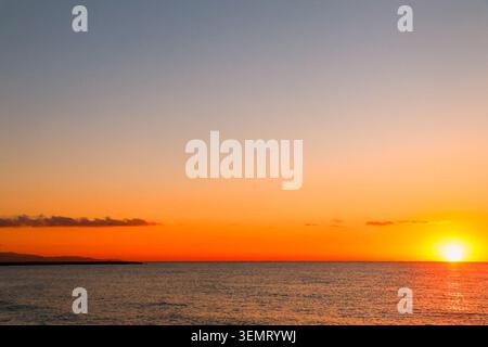 Großer Panoramaaufgang auf dem Ozean mit leuchtendem orangefarbenem Himmel und ruhigem Horizont am Meer während der goldenen Stunde. Stockfoto