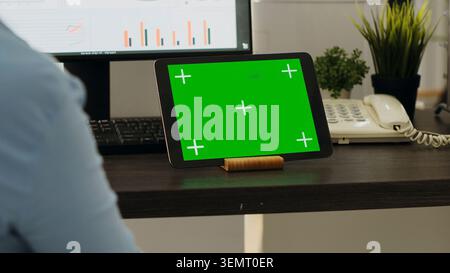 Frau arbeitet am Schreibtisch und verwendet moderne Gadget, um Green Screen Display zu präsentieren, Probleme im Coworking Space zu lösen, wobei junge Mitarbeiter sich eine leere Mockup Chroma Key Vorlage ansehen. Stockfoto
