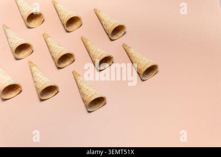 Leere Waffelkegel auf beigefarbenem Hintergrund in diagonalem Muster, Draufsicht, minimalistischer Stil. Stockfoto
