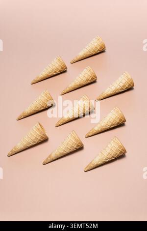 Leere Waffelkegel auf beigefarbenem Hintergrund, die ein einfaches und minimalistisches Muster schaffen. Stockfoto