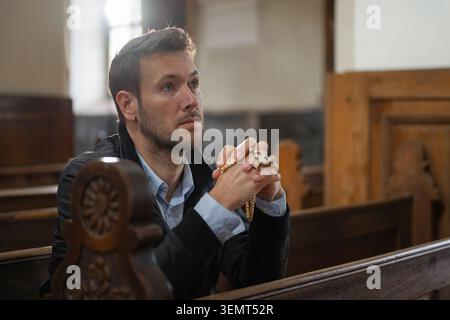 Mann im Gebet, Hände gefaltet im Gebet, während er einen Rosenkranz hält, mächtiges Symbol des Glaubens, der Kraft, der Hingabe und einer Geste des Trostes. Stockfoto