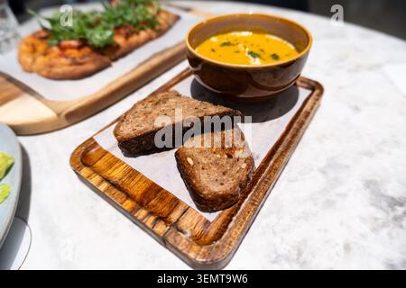 Nahaufnahme einer cremigen Orangensuppe in Keramikschale mit rustikalen Vollkornbrotscheiben auf Holz Stockfoto