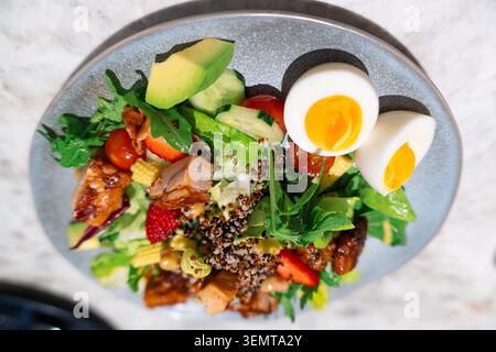 Blick von oben auf einen lebendigen gesunden Salat mit pochierten Eiern, Avocado, Quinoa, Kirschtomaten und Stockfoto