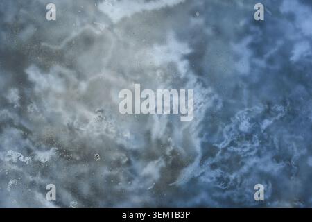 Gefrorene Gekräuselte Wasseroberfläche Mit Wolkenbildung In Flachem Puddle Close Up Makro Mit Diffusen Lichtreflexen Und Strukturierten Lichtdurchlässigen Schichten Auf Kaltem Boden. Stockfoto