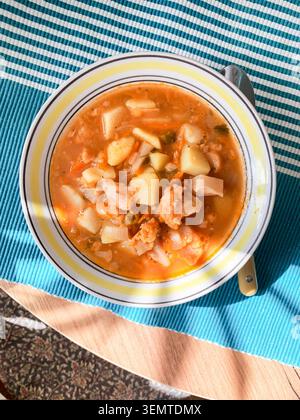 Eine Schüssel Suppe mit Kartoffeln, Linsen und Blumenkohl steht auf einem Tisch, der mit einem gestreiften Tuch bedeckt ist, und genießt tagsüber das Licht von oben. Stockfoto