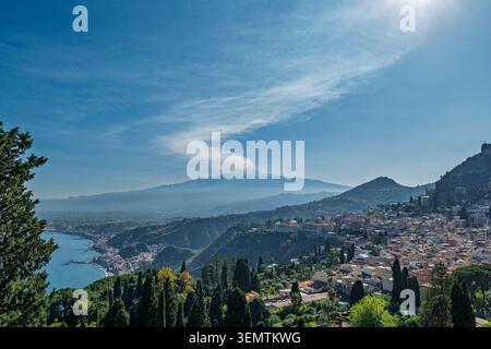 Panoramablick auf Taormina, die historische Stadt auf einem Hügel an der Ostküste Siziliens, Italien, mit dem aktiven Vulkan Ätna, der eine Pflaume ausstrahlt Stockfoto