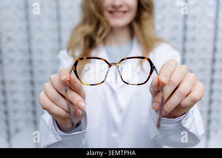 Ein lächelnder Optiker präsentiert dem Kunden eine stilvolle Brille, die in einem gut beleuchteten optischen Geschäft Optionen für Menschen mit schlechter Sicht bietet. Stockfoto