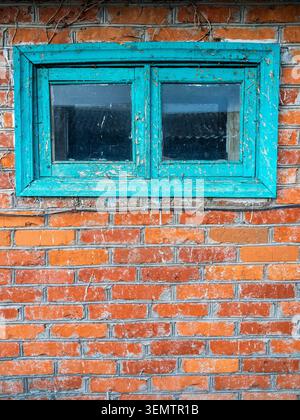 Die rote Ziegelwand der alten Hütte wurde von efeu gereinigt und mit einem schäbigen kleinen Fensterrahmen, der im Dorf grün gestrichen wurde Stockfoto