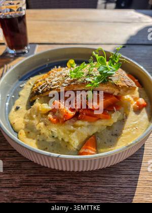 Gegrilltes Lachsfilet wird auf einem cremigen Gemüsebrei mit Karottenstücken serviert und mit frischen Kräutern belegt Stockfoto
