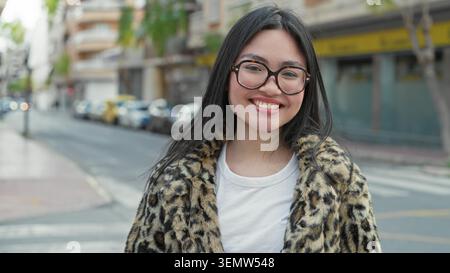 Frau mit Brille, lächelnd und über die Schulter schauend, Leopardenmantel auf der Straße sichtbar; Selbstvertrauen urbaner. Stockfoto